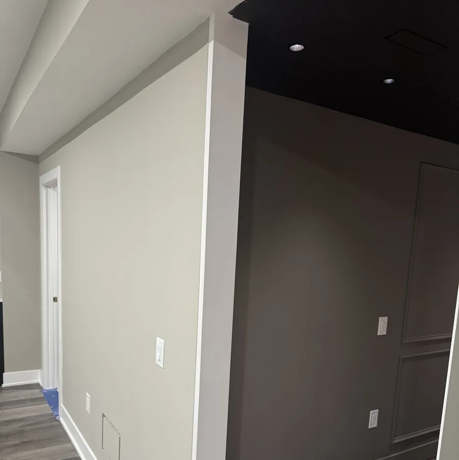 Finished basement hallway junction — beige painted wall meets dark charcoal moulding accent zone, premium LVP flooring running through