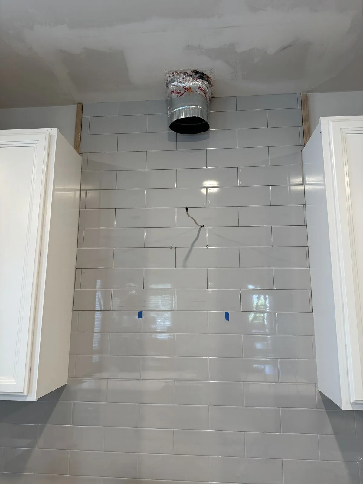 Tile extension in progress to ceiling height with duct stub visible — West Chester kitchen mid-installation